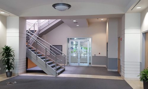 Modern building lobby with a staircase and glass entrance doors.