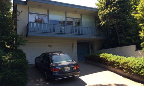 A two-story house with a car parked in the driveway under a balcony.